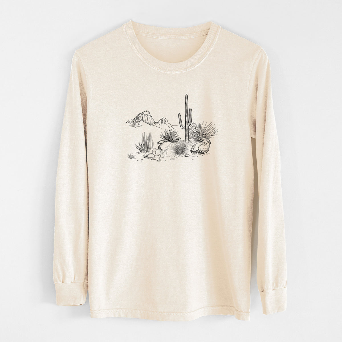 Ivory Comfort Colors long sleeve shirt laid flat, printed with a black ink desert scene with a saguaro cactus, agave, rocks and distant mountains.