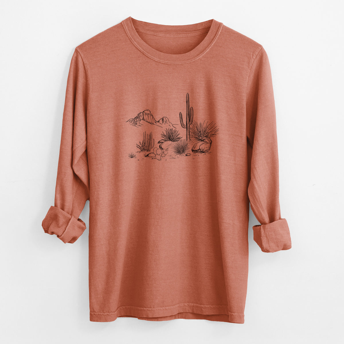 Yam burnt orange Comfort Colors long sleeve shirt laid flat with the cuffs rolled, printed with a black ink desert scene with a saguaro cactus, agave, rocks and distant mountains.