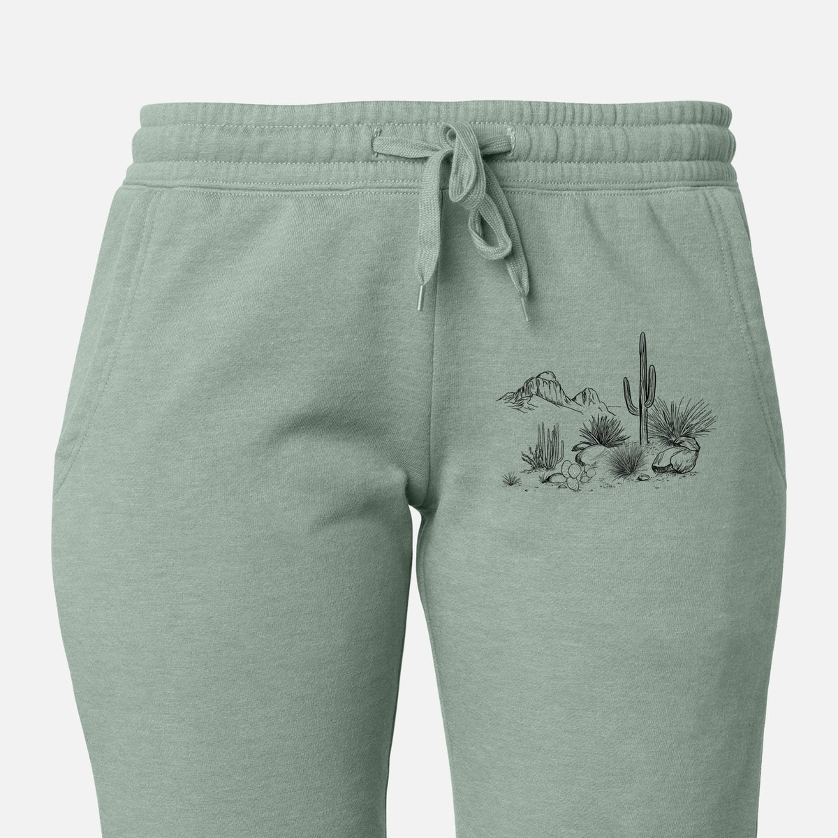 Front of sage green Cali Wave sweatpants, printed with a black ink desert scene with a saguaro cactus, agave, rocks and distant mountains on the leg.