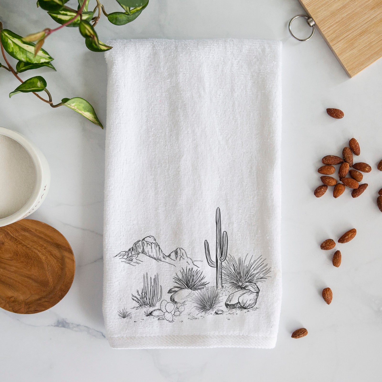 White hand towel printed with a black ink desert scene with a saguaro cactus, agave, rocks and distant mountains.