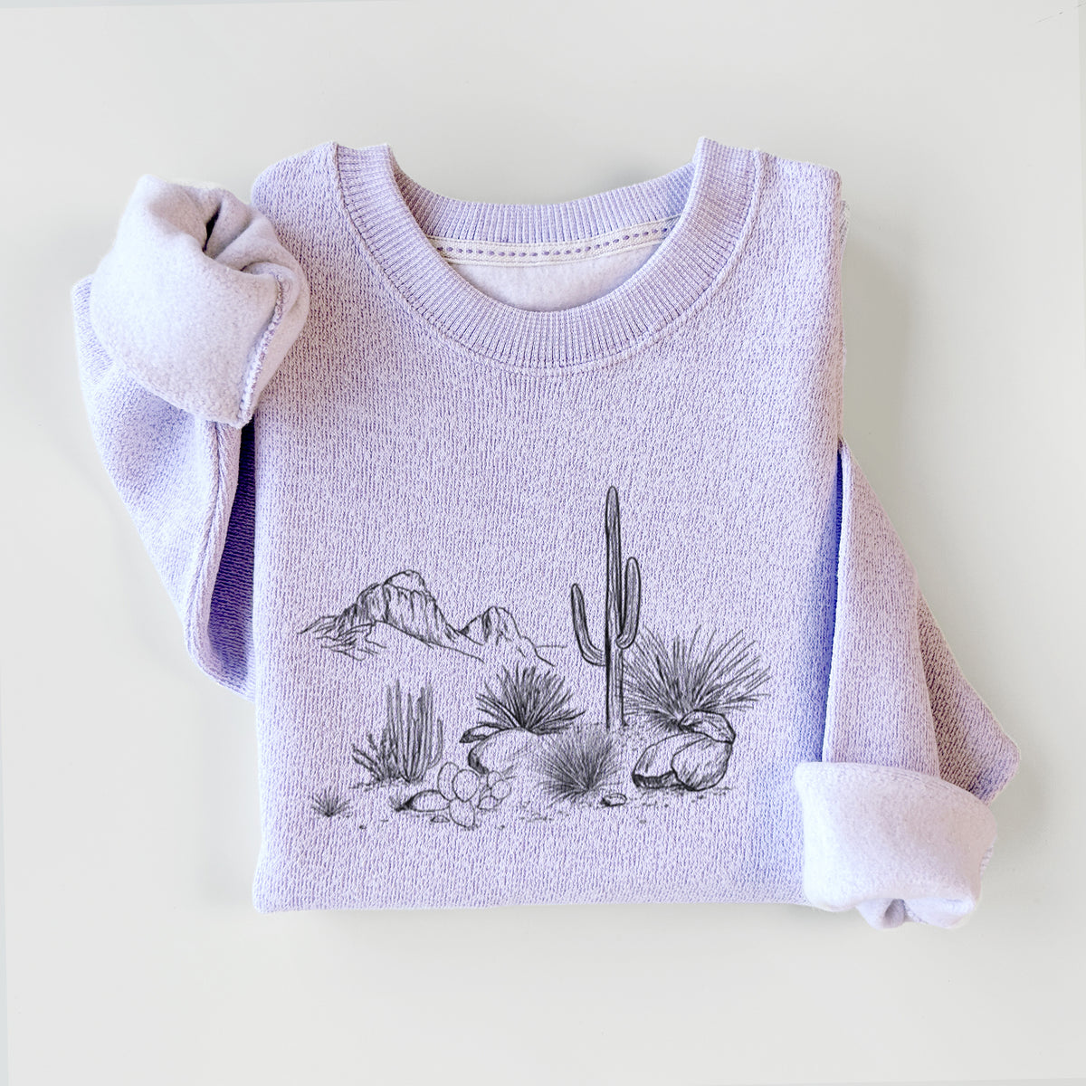 Ice purple knit sweatshirt printed with a black ink desert scene with a saguaro cactus, agave, rocks and distant mountains, styled flat.