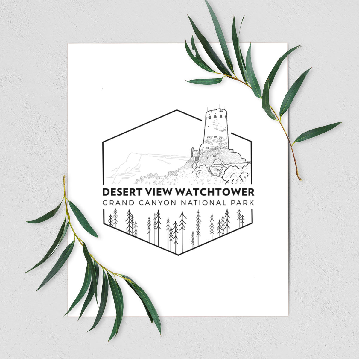 Art print of a black line art badge of the Desert View Watchtower above pine trees, with the words Desert View Watchtower, Grand Canyon National Park, shown with eucalyptus leaves.