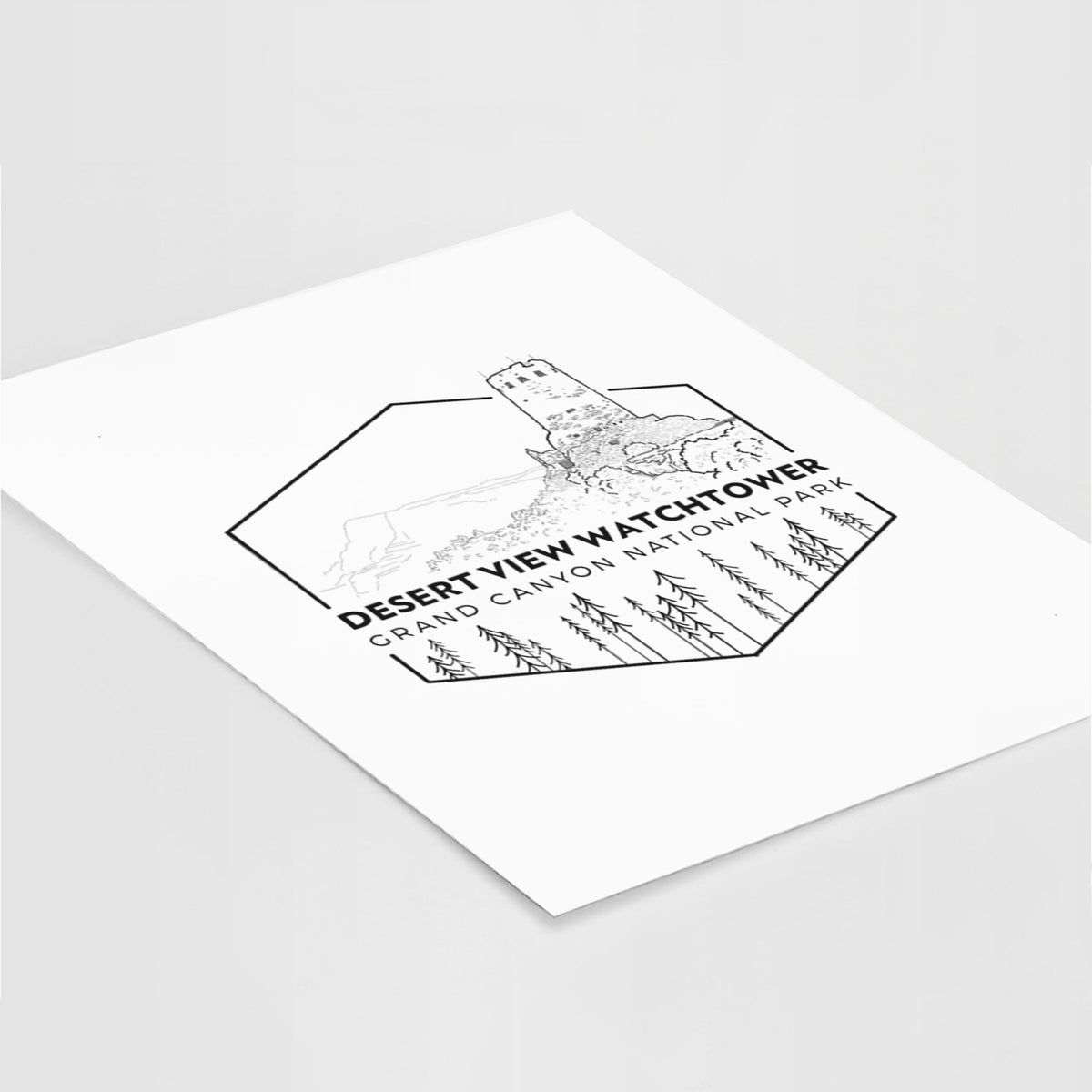 Art print of a black line art badge of the Desert View Watchtower above pine trees, with the words Desert View Watchtower, Grand Canyon National Park, lying at an angle on a white surface.
