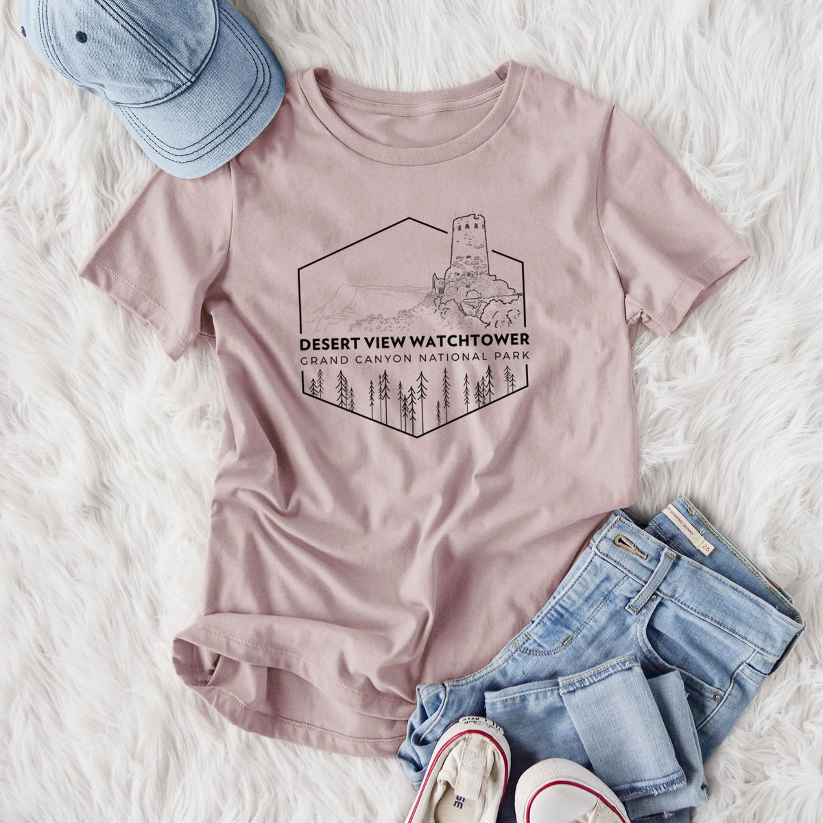 Women's relaxed fit cotton t-shirt printed with a black line art badge of the Desert View Watchtower above pine trees, with the words Desert View Watchtower, Grand Canyon National Park, styled flat on a white faux fur rug with jeans.