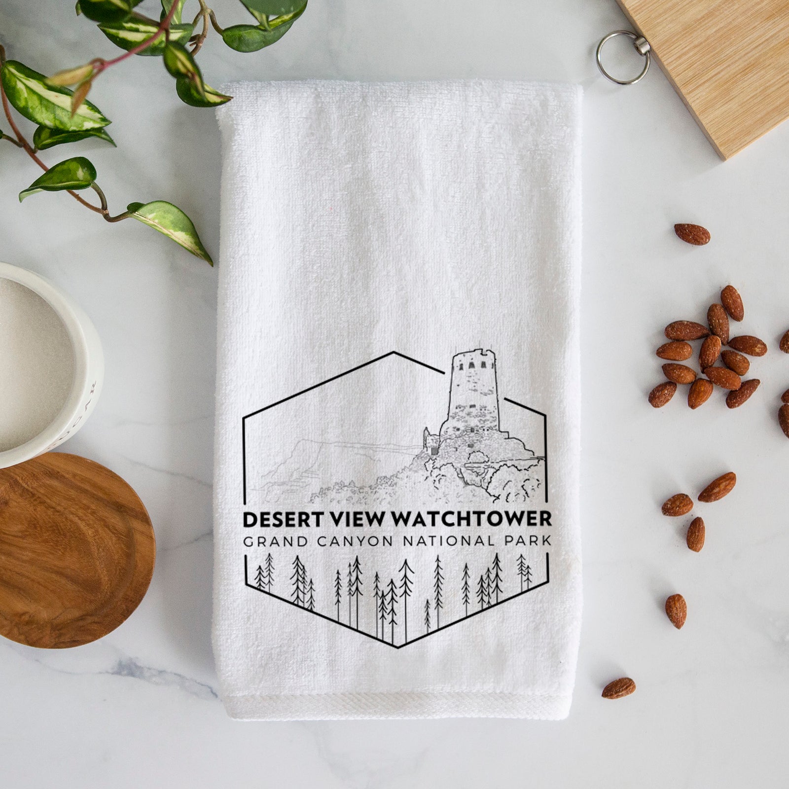 White hand towel printed with a black line art badge of the Desert View Watchtower above pine trees, with the words Desert View Watchtower, Grand Canyon National Park.