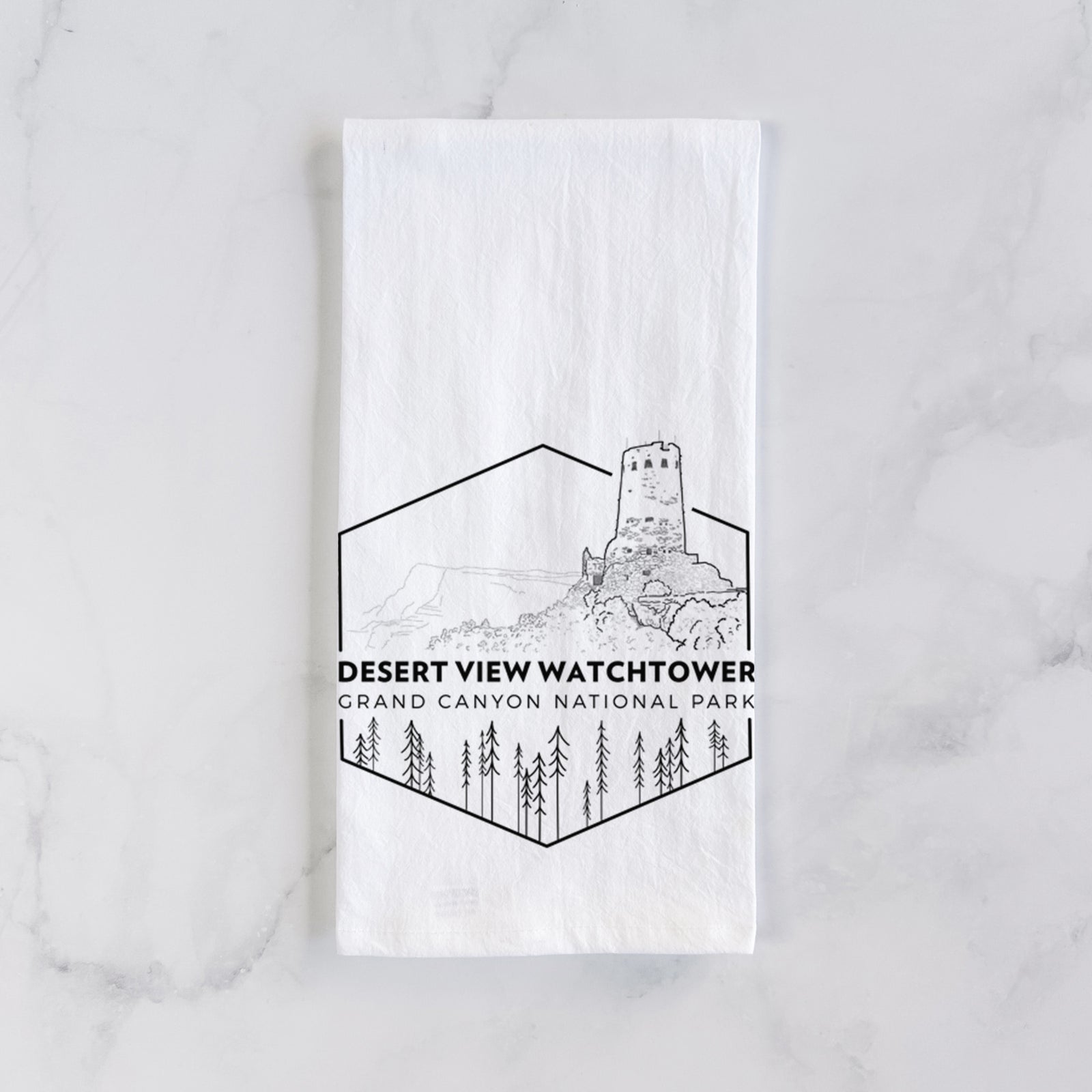 White cotton tea towel printed with a black line art badge of the Desert View Watchtower above pine trees, with the words Desert View Watchtower, Grand Canyon National Park, on a marble counter beside a round wooden cutting board and greenery.