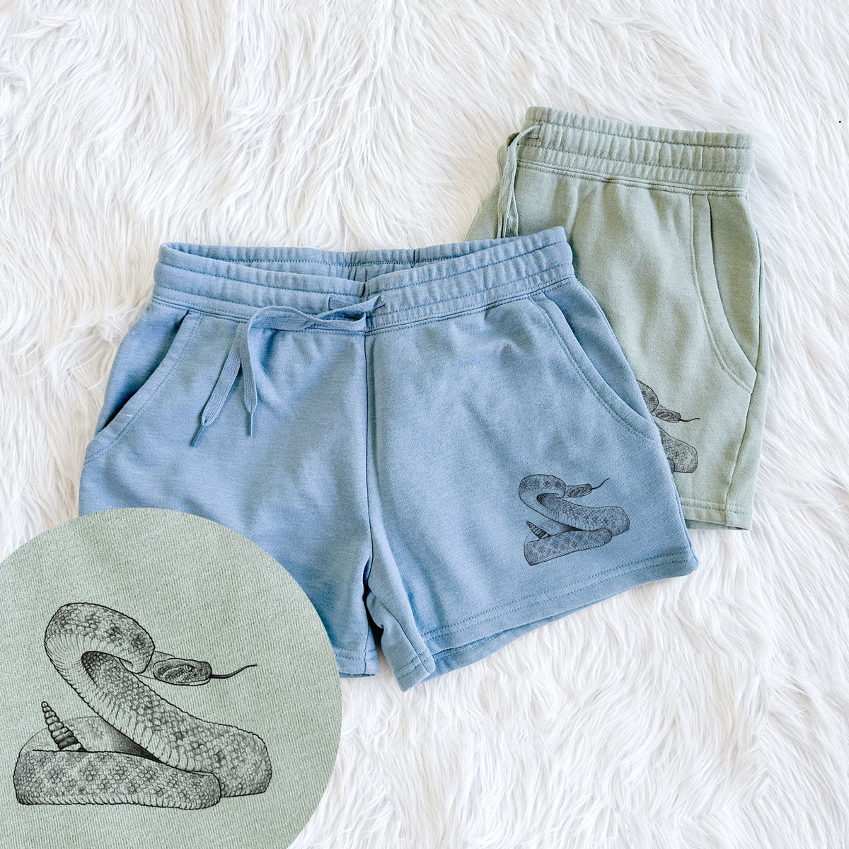 Two pairs of Cali Wave shorts in different colors printed with a detailed black ink illustration of a coiled diamondback rattlesnake, with a close-up of the print.