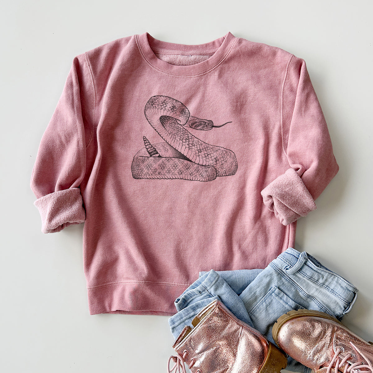 Youth crewneck sweatshirt printed with a detailed black ink illustration of a coiled diamondback rattlesnake, styled flat with jeans and boots.