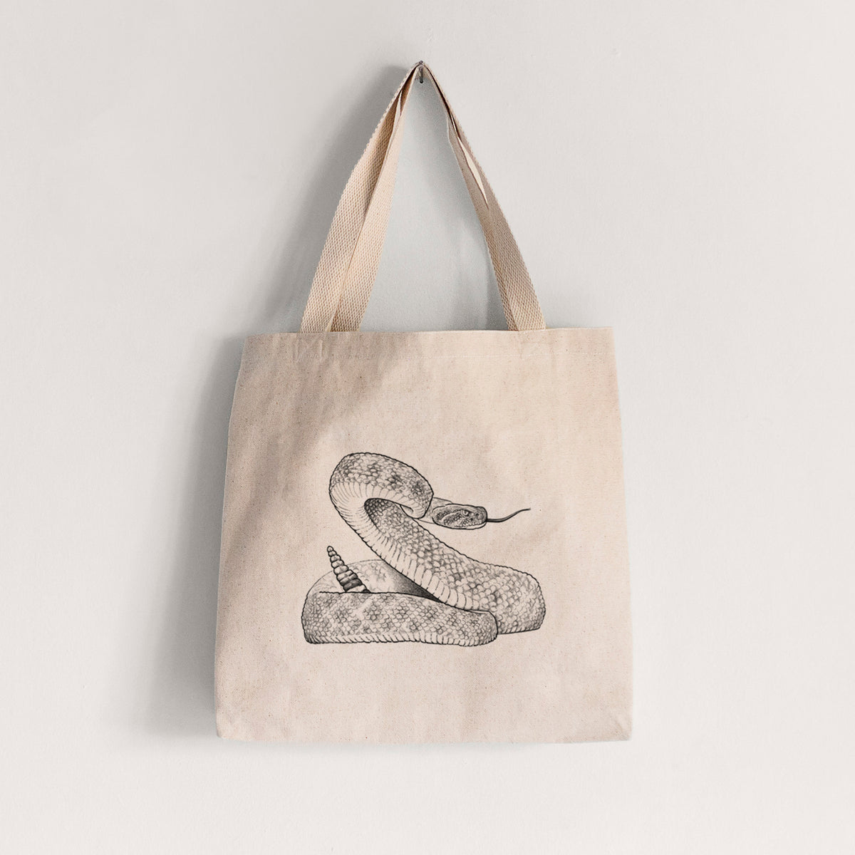 Natural canvas tote bag printed with a detailed black ink illustration of a coiled diamondback rattlesnake.