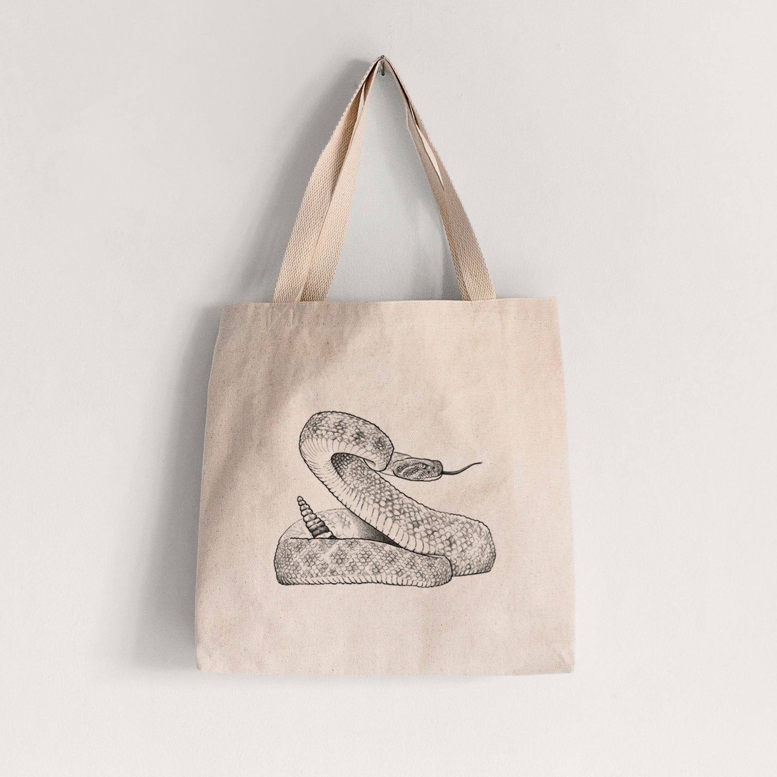 Natural canvas tote bag printed with a detailed black ink illustration of a coiled diamondback rattlesnake.