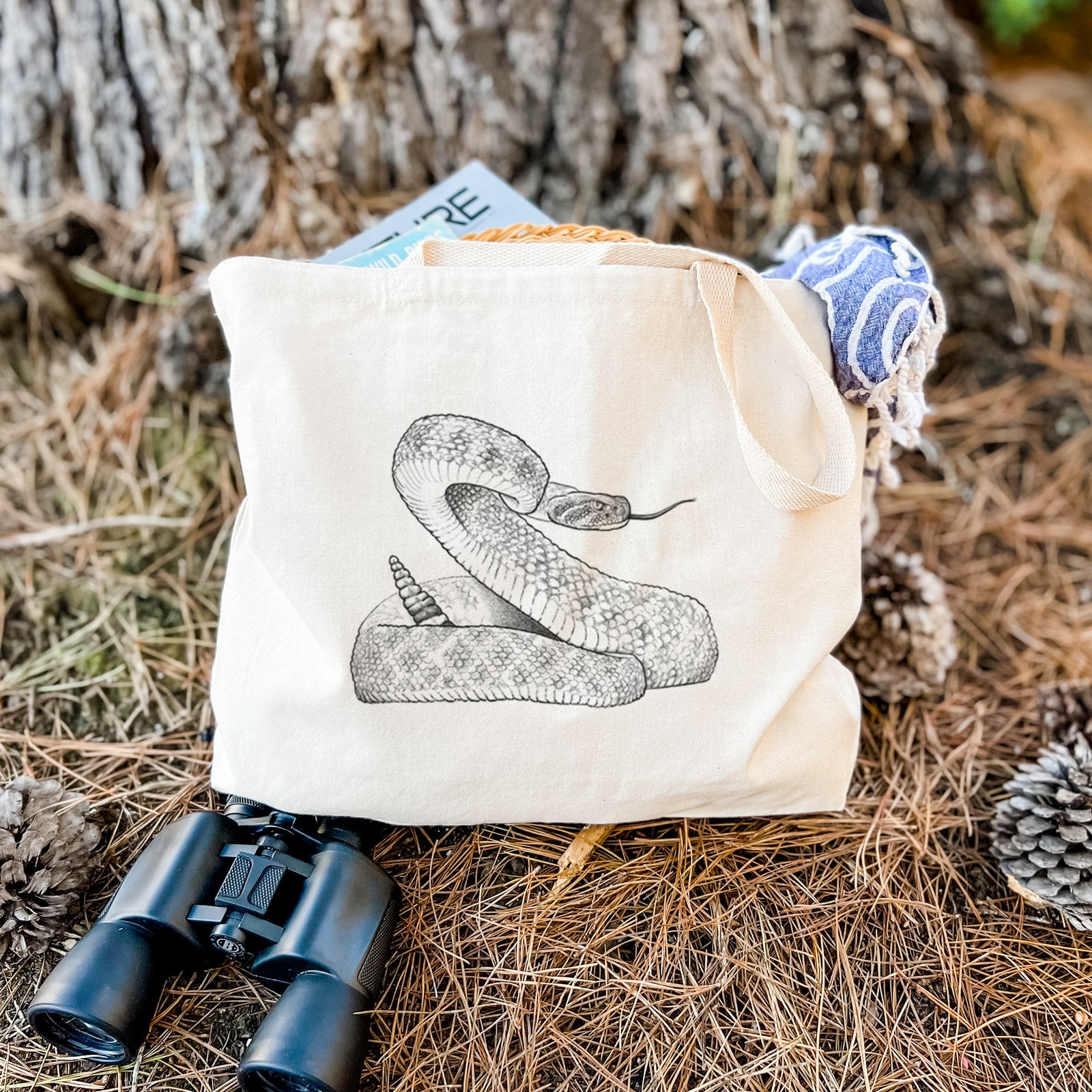 Natural canvas tote bag printed with a detailed black ink illustration of a coiled diamondback rattlesnake.