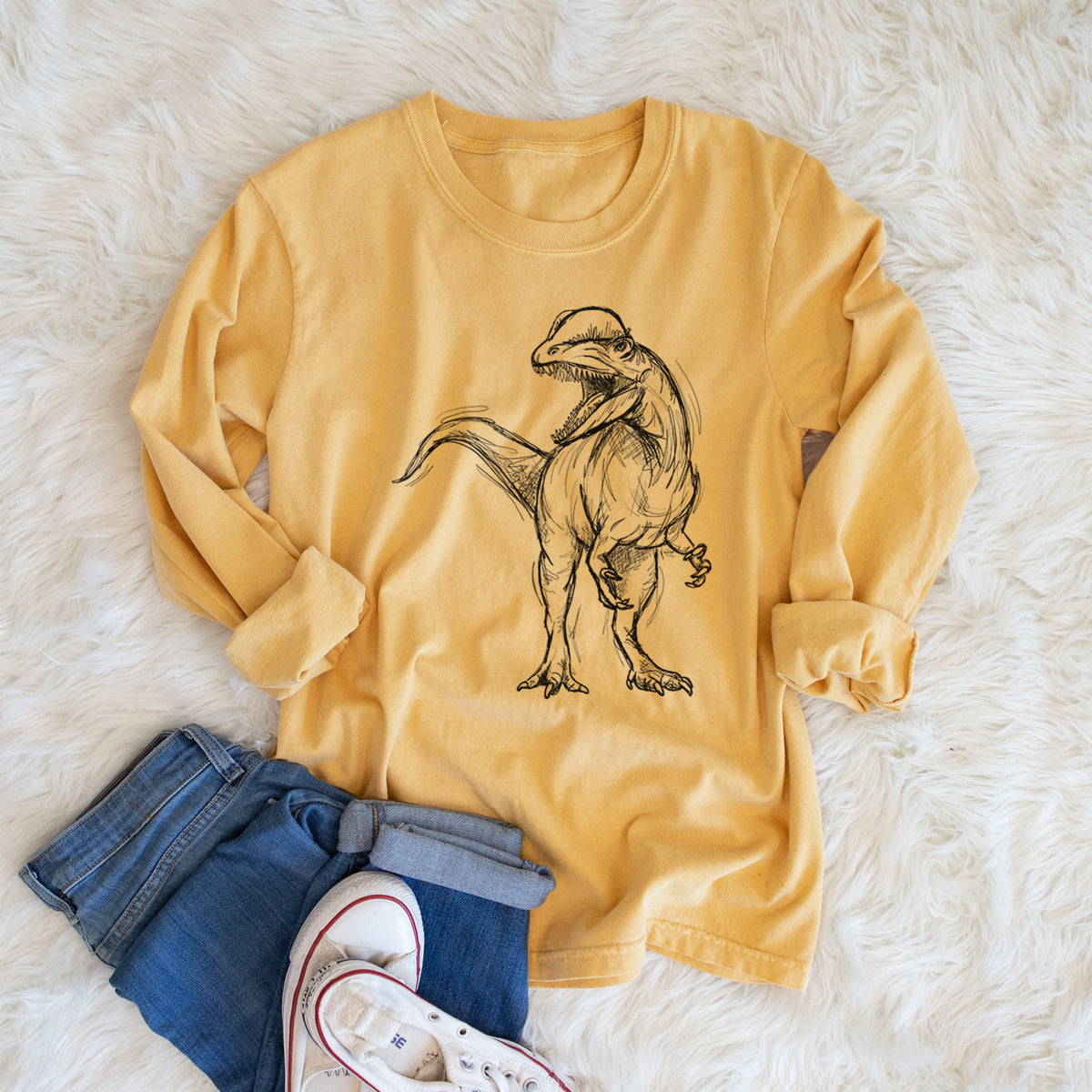 Golden wheat yellow Comfort Colors long sleeve shirt printed with a black ink illustration of a Dilophosaurus with its neck frill, walking, shown in a lifestyle photo.