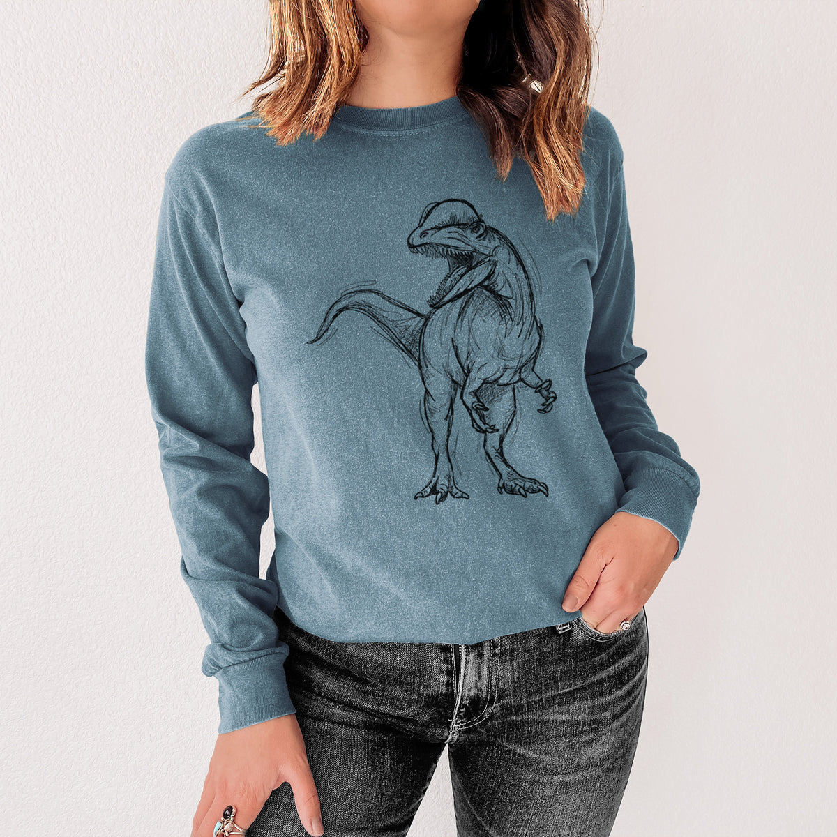 Steel blue Comfort Colors long sleeve shirt printed with a black ink illustration of a Dilophosaurus with its neck frill, walking, shown in a lifestyle photo.