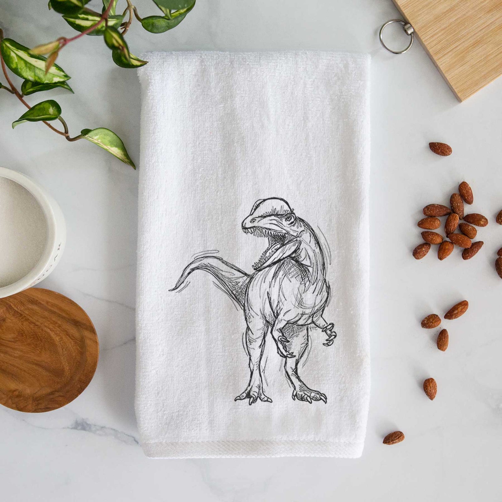 White hand towel printed with a black ink illustration of a Dilophosaurus with its neck frill, walking.