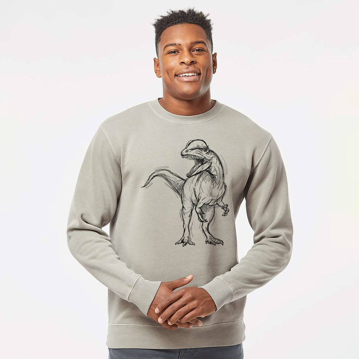 Model wearing a cement grey pigment dyed crewneck sweatshirt printed with a black ink illustration of a Dilophosaurus with its neck frill, walking.