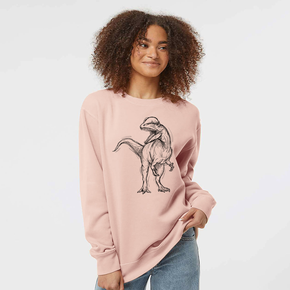 Model wearing a dusty pink pigment dyed crewneck sweatshirt printed with a black ink illustration of a Dilophosaurus with its neck frill, walking.
