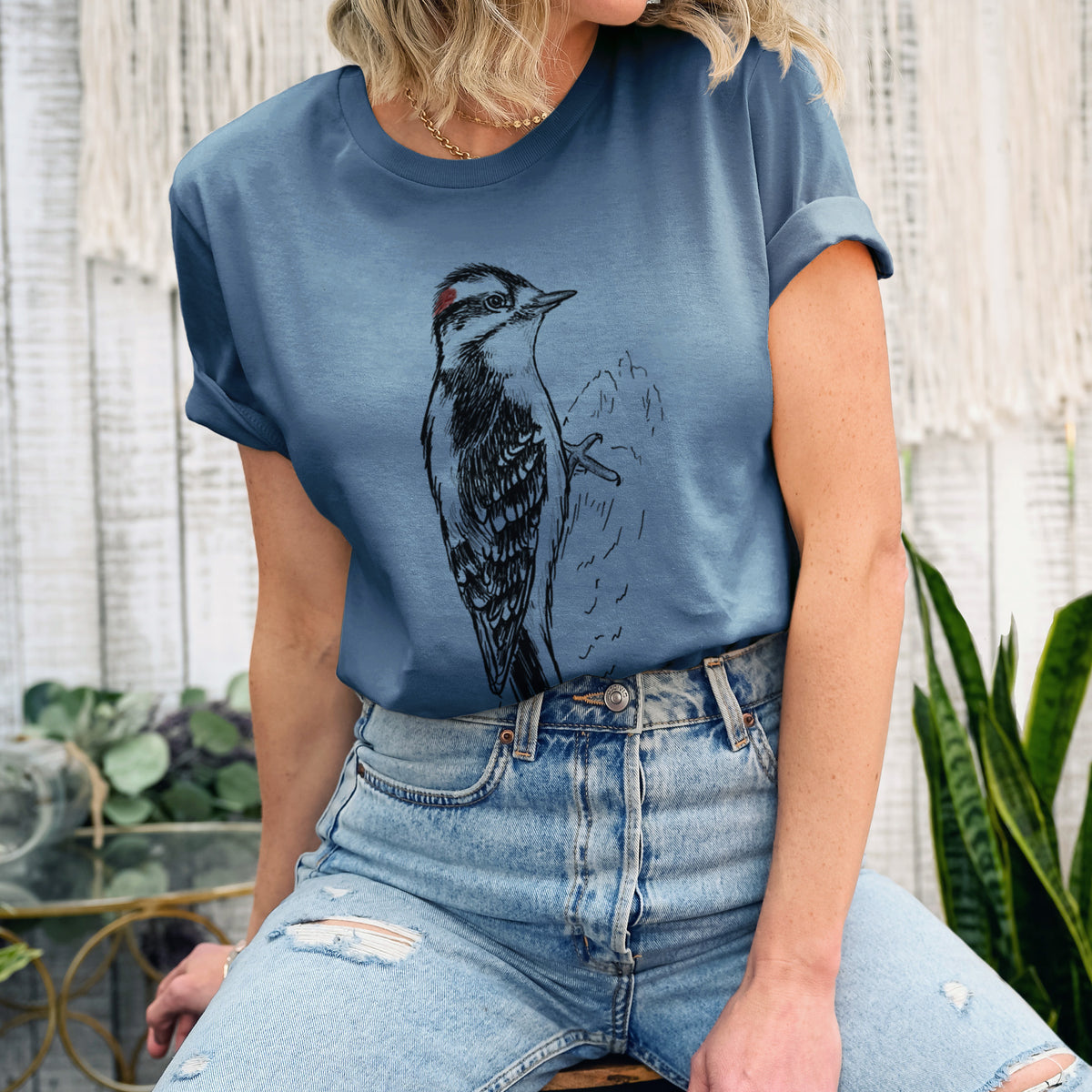 Woman wearing a steel blue lightweight cotton t-shirt printed with a detailed black ink illustration of a downy woodpecker clinging to a tree trunk.