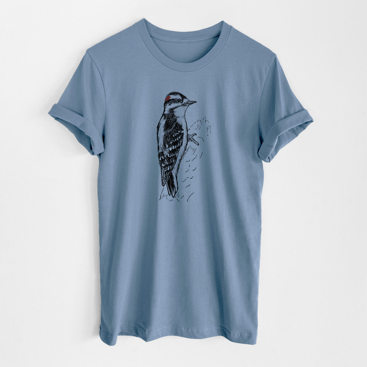 Steel blue lightweight cotton t-shirt laid flat, printed with a detailed black ink illustration of a downy woodpecker clinging to a tree trunk.