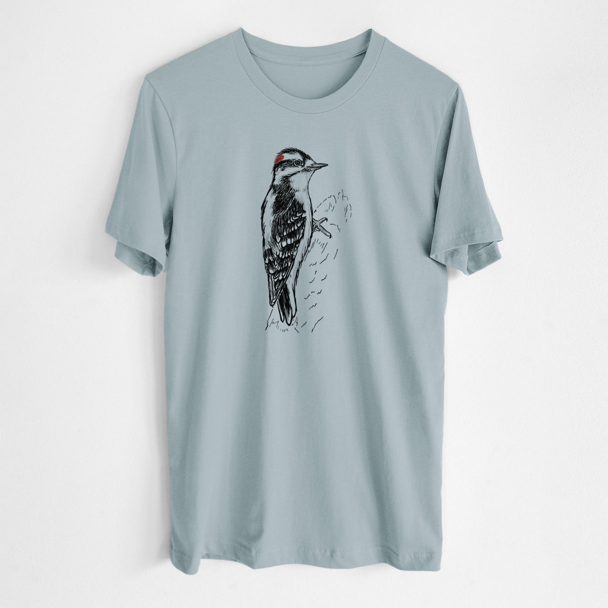 Vintage denim lightweight cotton t-shirt laid flat, printed with a detailed black ink illustration of a downy woodpecker clinging to a tree trunk.