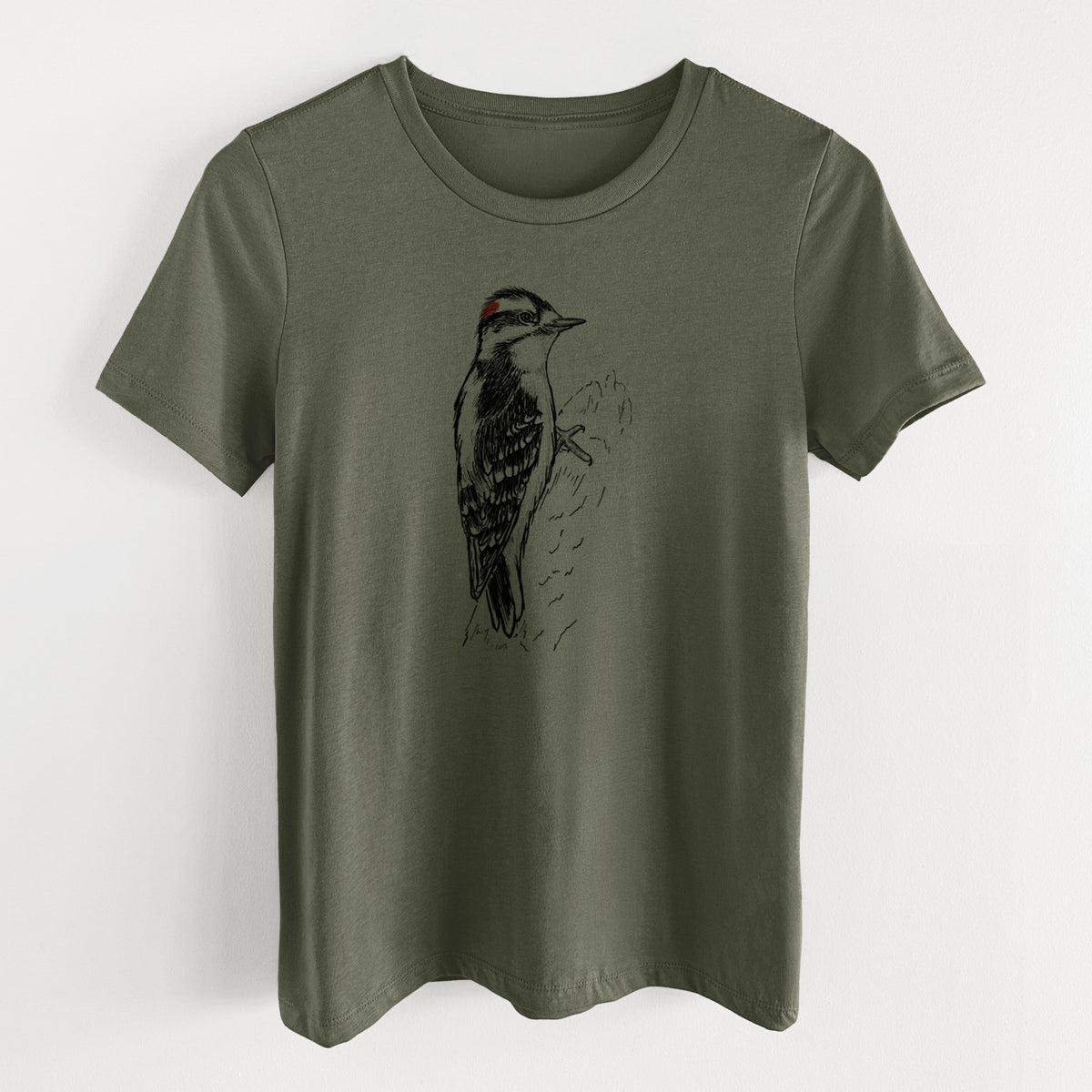 Military green women's relaxed fit cotton t-shirt laid flat, printed with a detailed black ink illustration of a downy woodpecker clinging to a tree trunk.