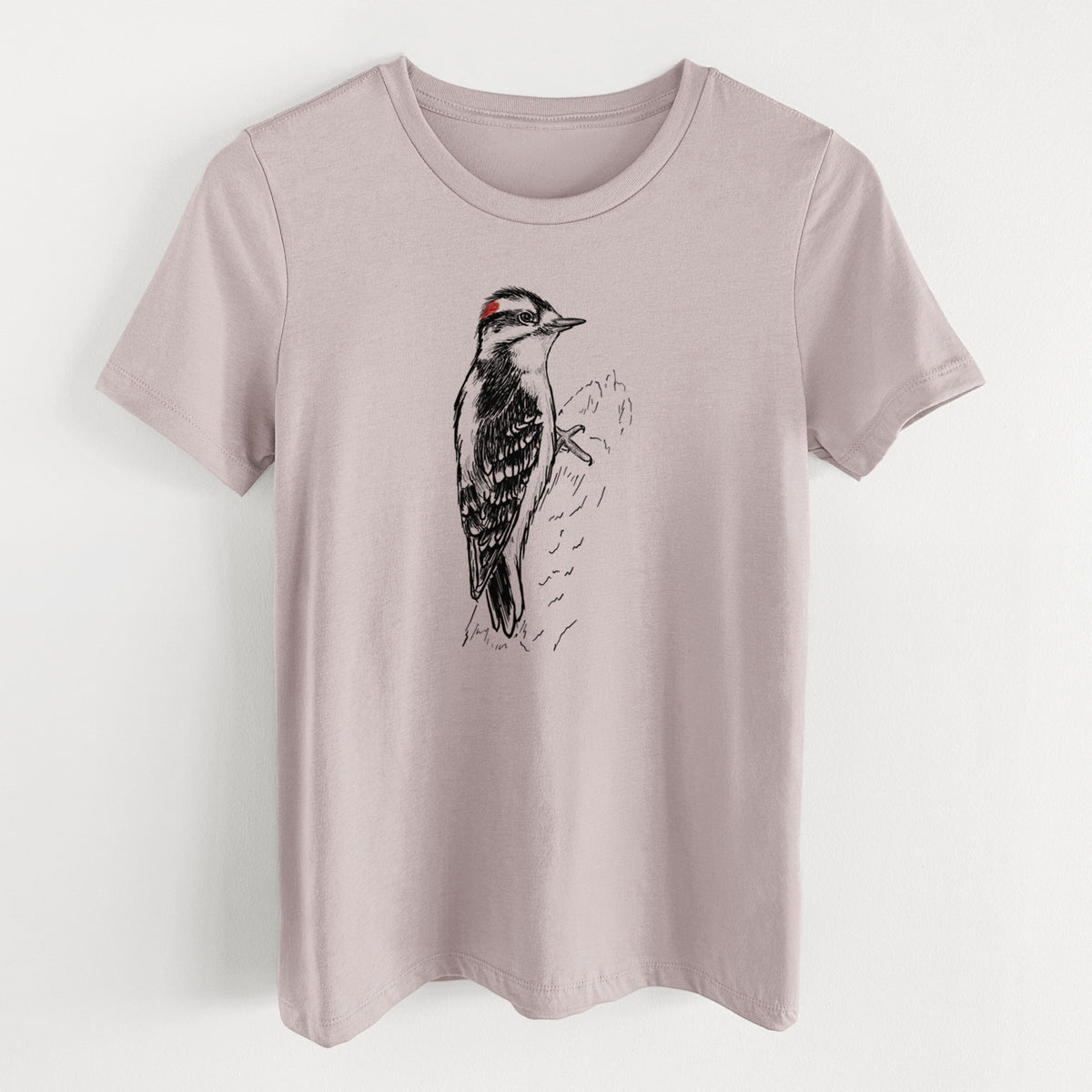 Pink gravel women's relaxed fit cotton t-shirt laid flat, printed with a detailed black ink illustration of a downy woodpecker clinging to a tree trunk.