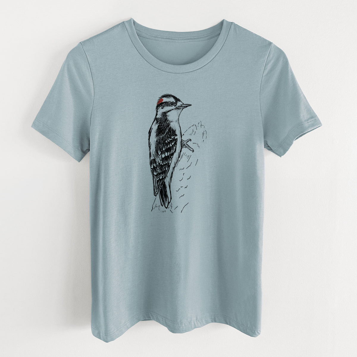 Vintage denim women's relaxed fit cotton t-shirt laid flat, printed with a detailed black ink illustration of a downy woodpecker clinging to a tree trunk.