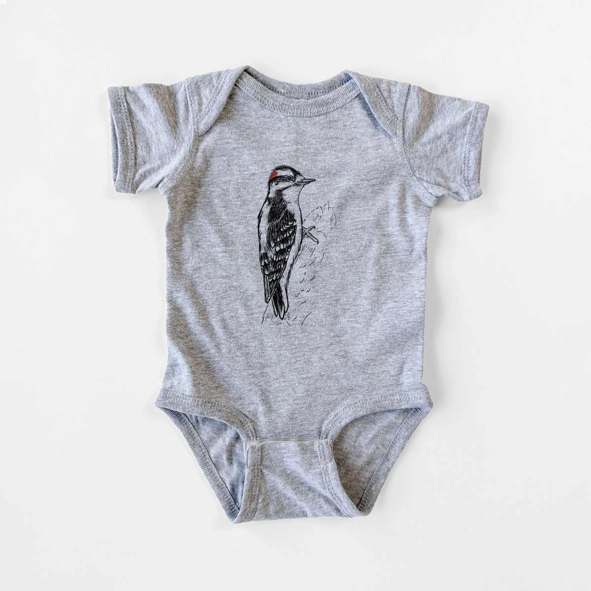Grey baby bodysuit laid flat, printed with a detailed black ink illustration of a downy woodpecker clinging to a tree trunk.