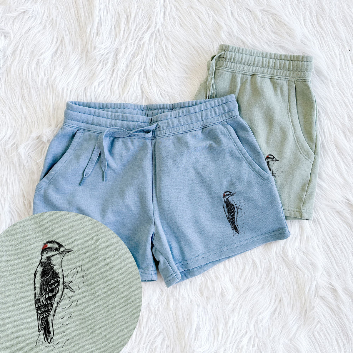 Two pairs of Cali Wave shorts in different colors printed with a detailed black ink illustration of a downy woodpecker clinging to a tree trunk, with a close-up of the print.