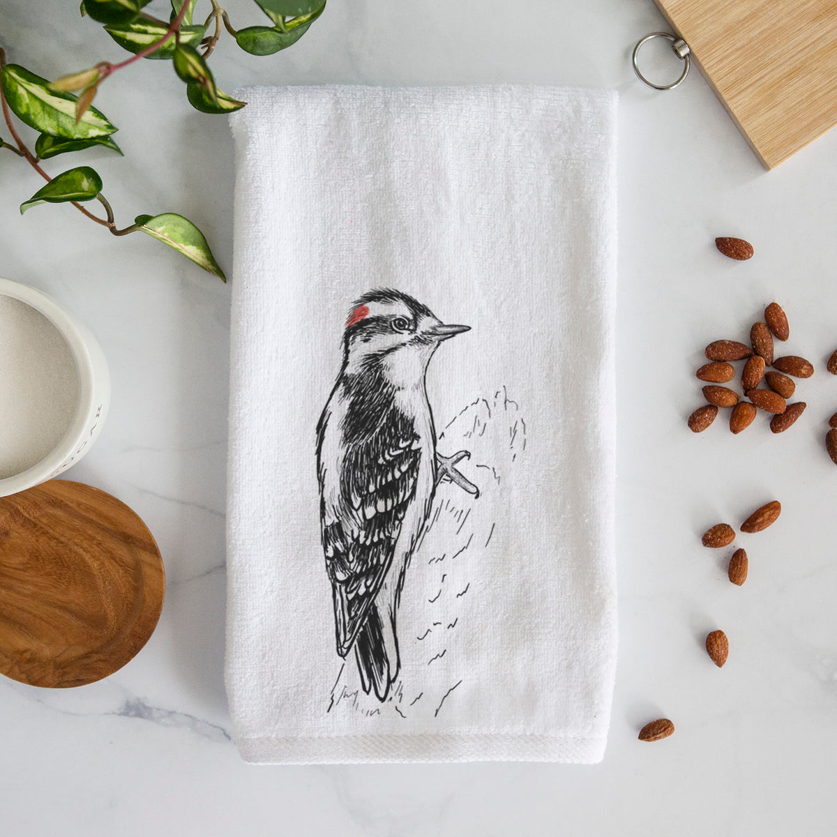 White hand towel printed with a detailed black ink illustration of a downy woodpecker clinging to a tree trunk.