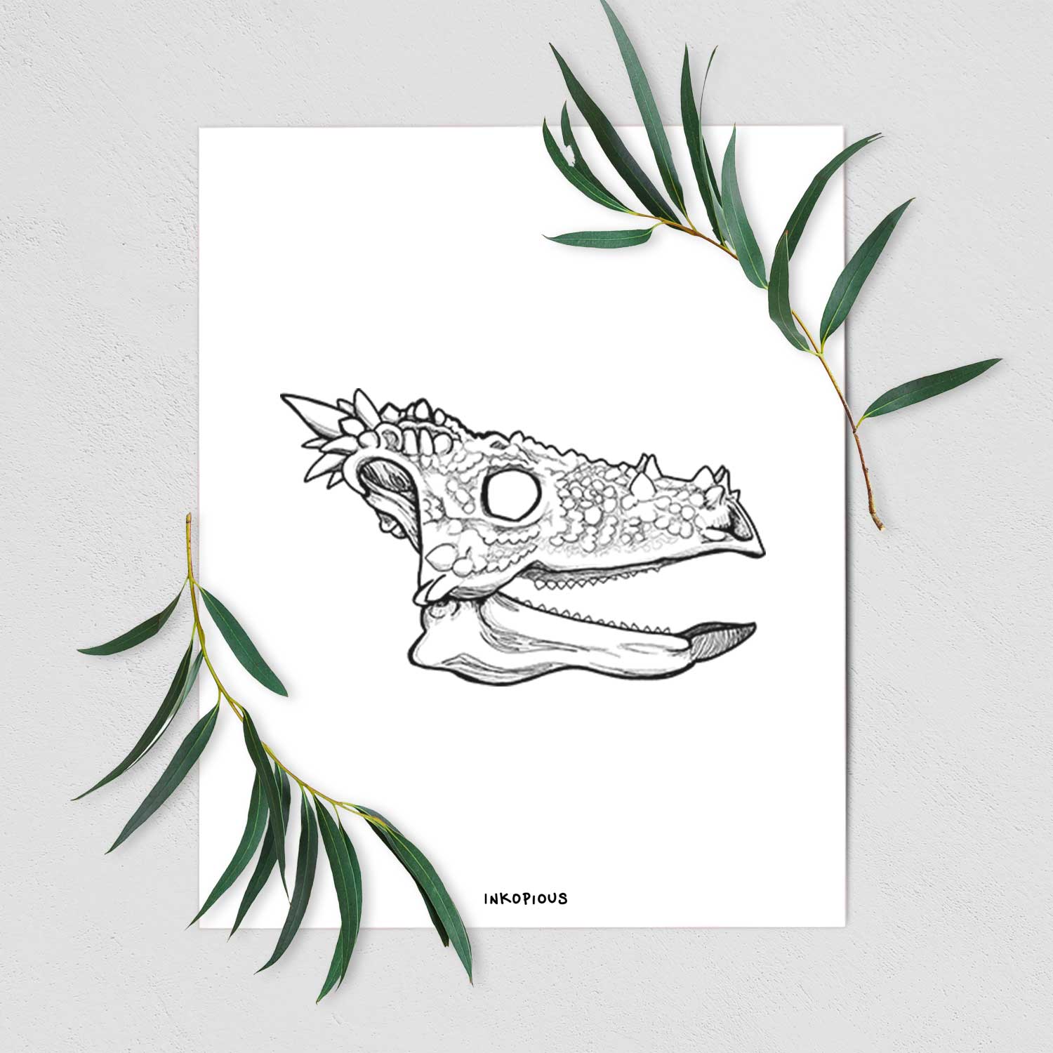 Art print of a black ink illustration of a spiky Dracorex dinosaur skull, shown with eucalyptus leaves.