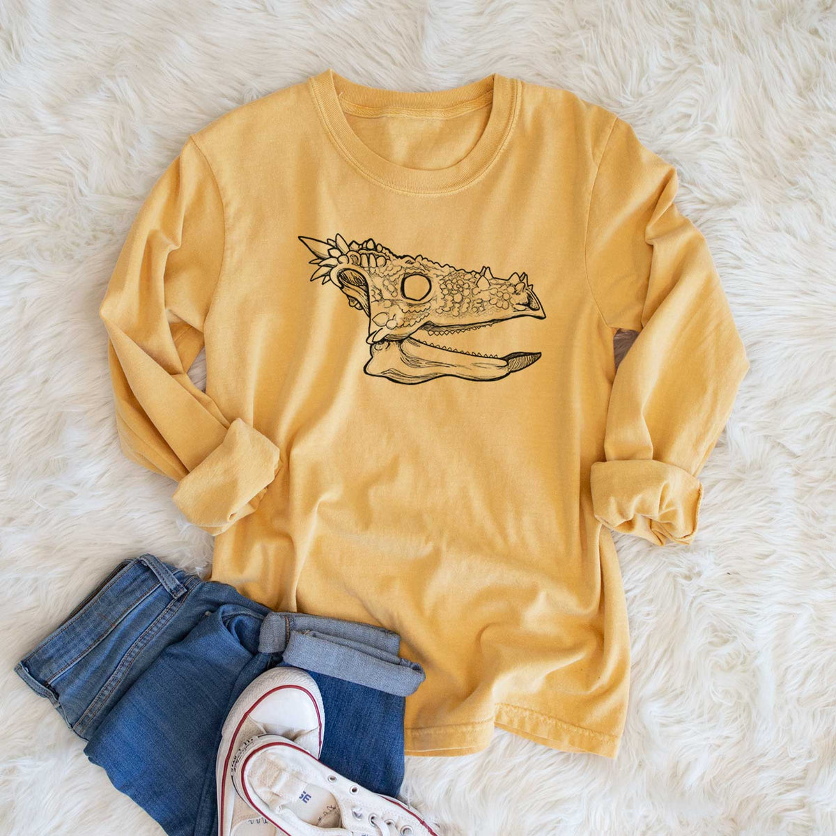 Golden wheat yellow Comfort Colors long sleeve shirt printed with a black ink illustration of a spiky Dracorex dinosaur skull, shown in a lifestyle photo.