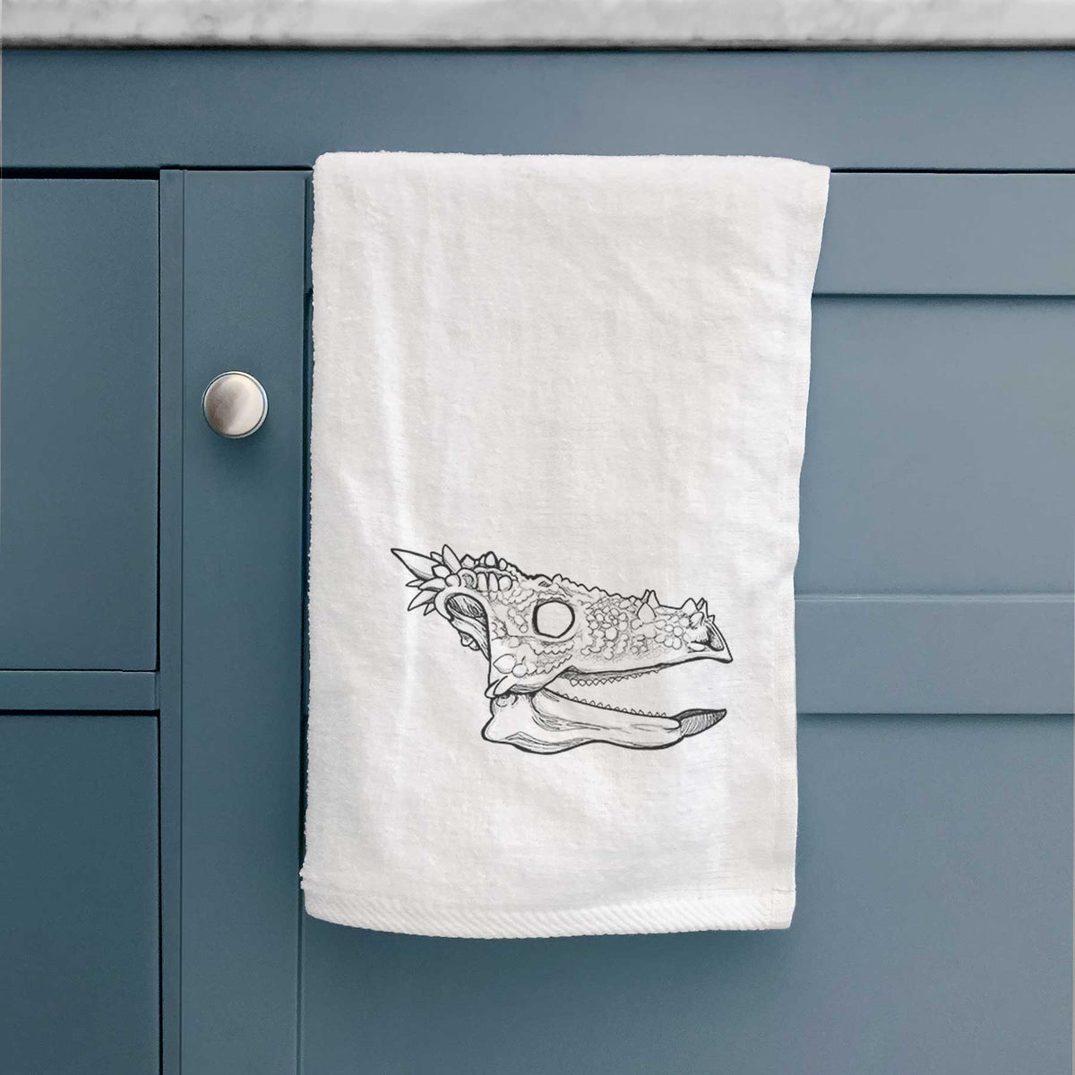 White hand towel printed with a black ink illustration of a spiky Dracorex dinosaur skull.