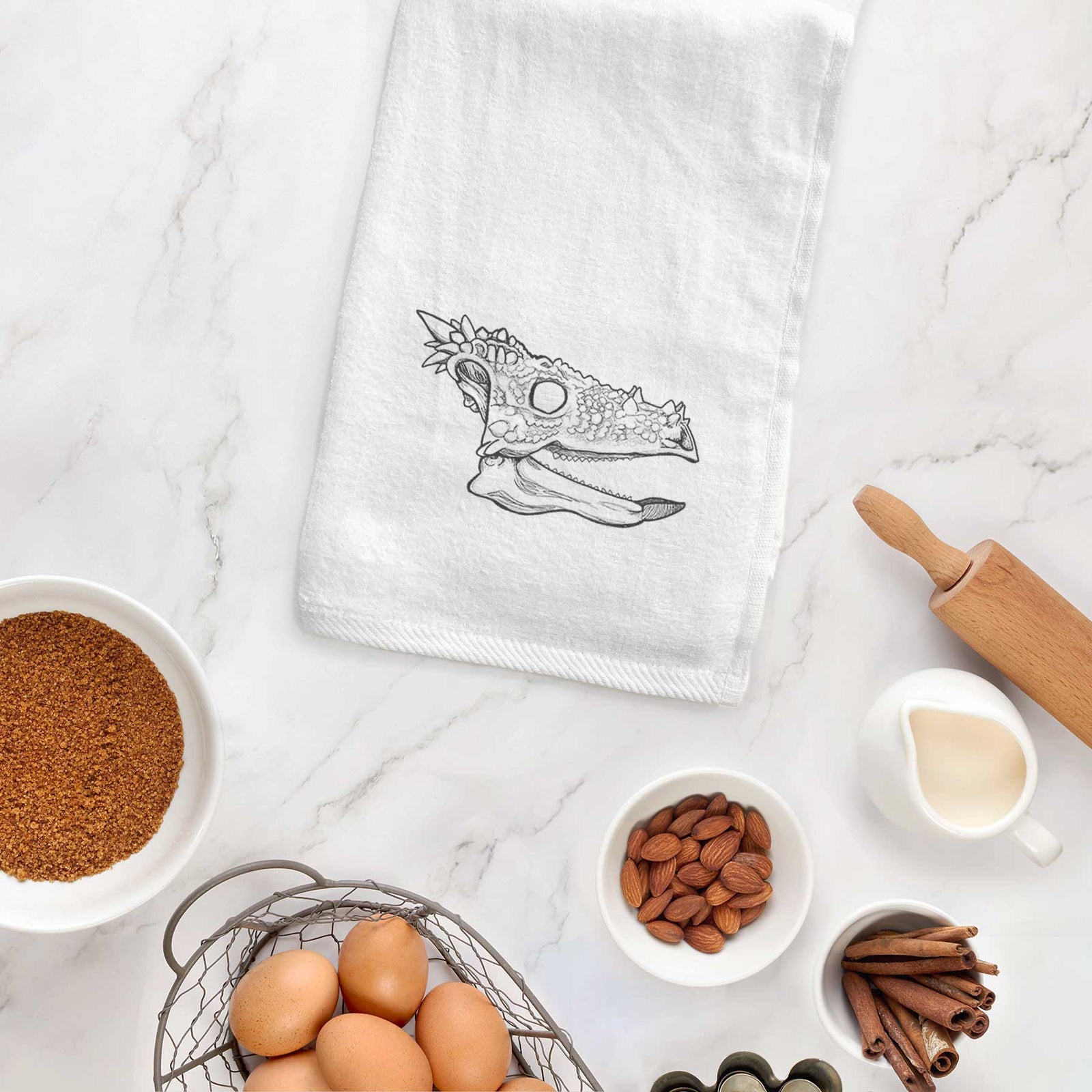 White hand towel printed with a black ink illustration of a spiky Dracorex dinosaur skull.