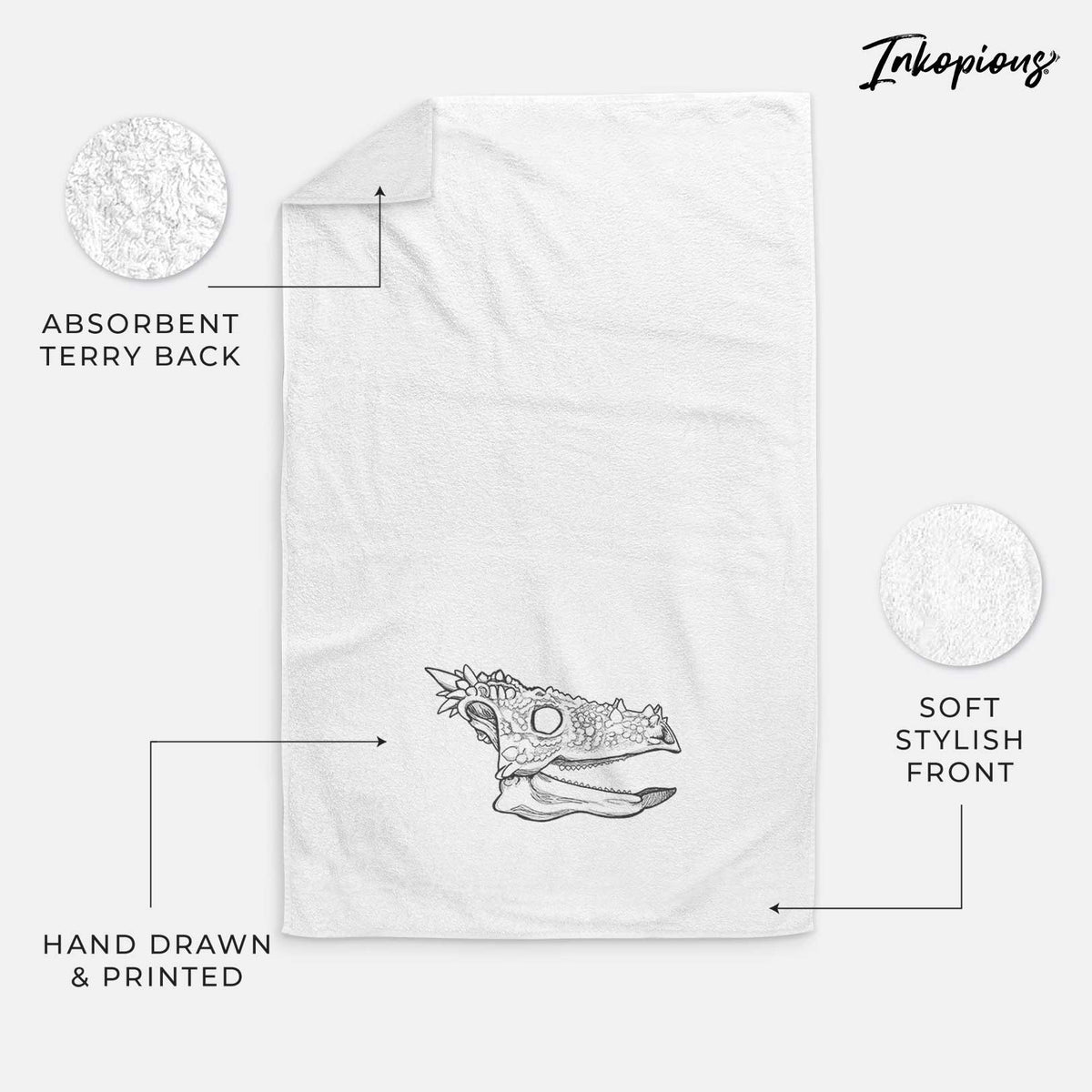 White hand towel printed with a black ink illustration of a spiky Dracorex dinosaur skull.