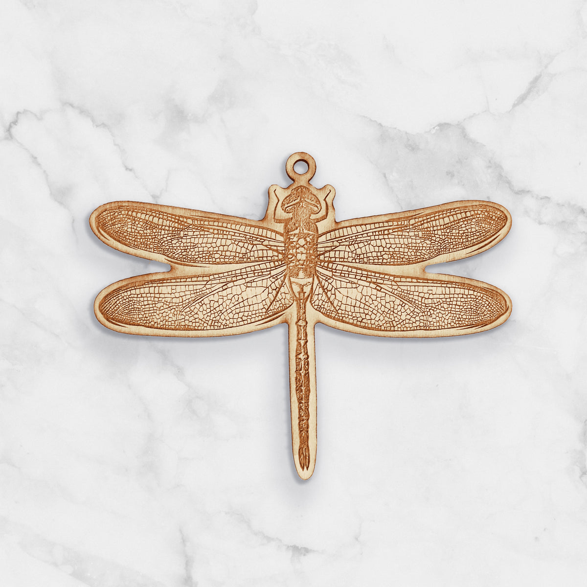 Wooden ornament featuring a detailed engraving of a dragonfly with patterned wings, on a marble surface.