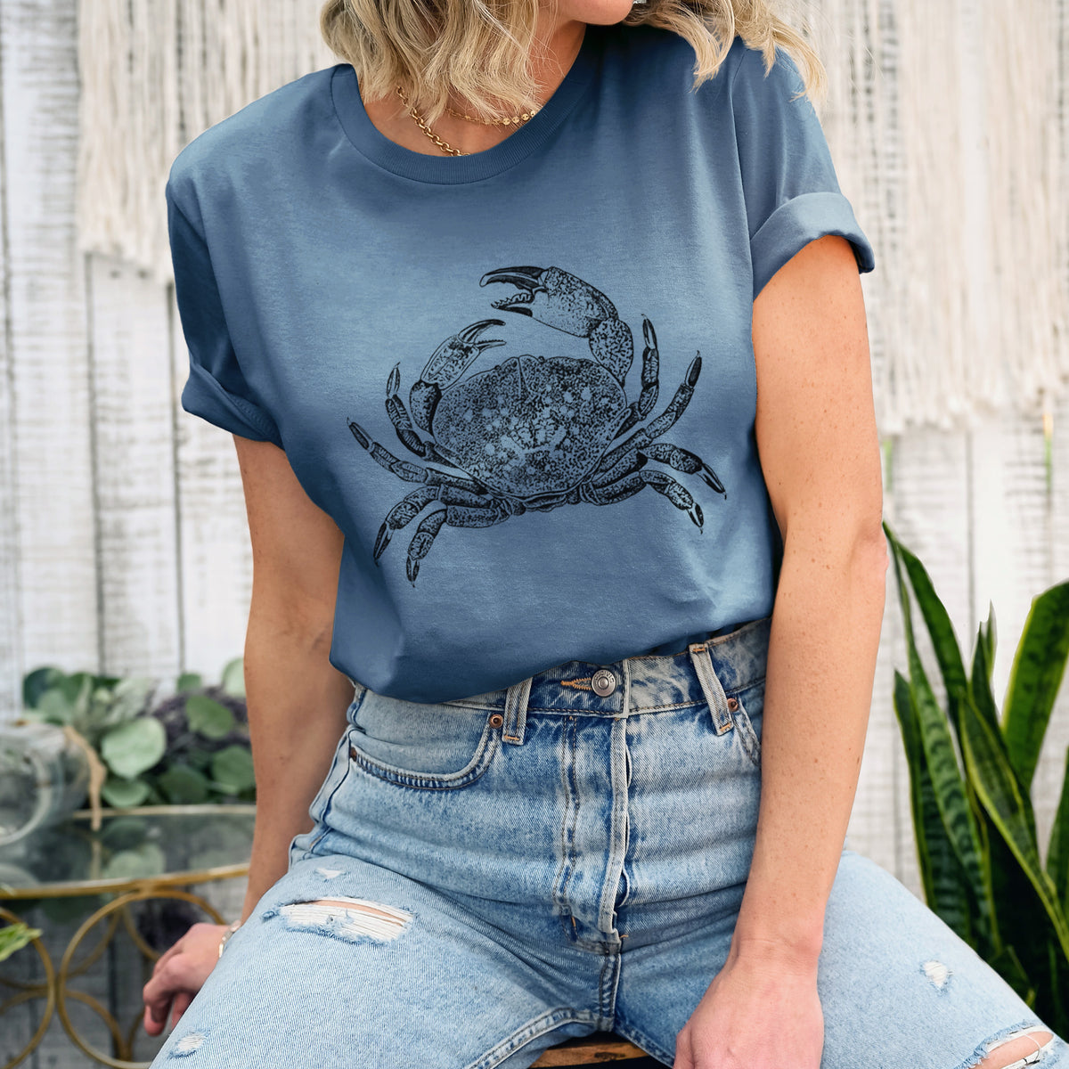 Woman wearing a steel blue lightweight cotton t-shirt printed with a detailed black ink illustration of a Dungeness crab with claws raised, seen from above.