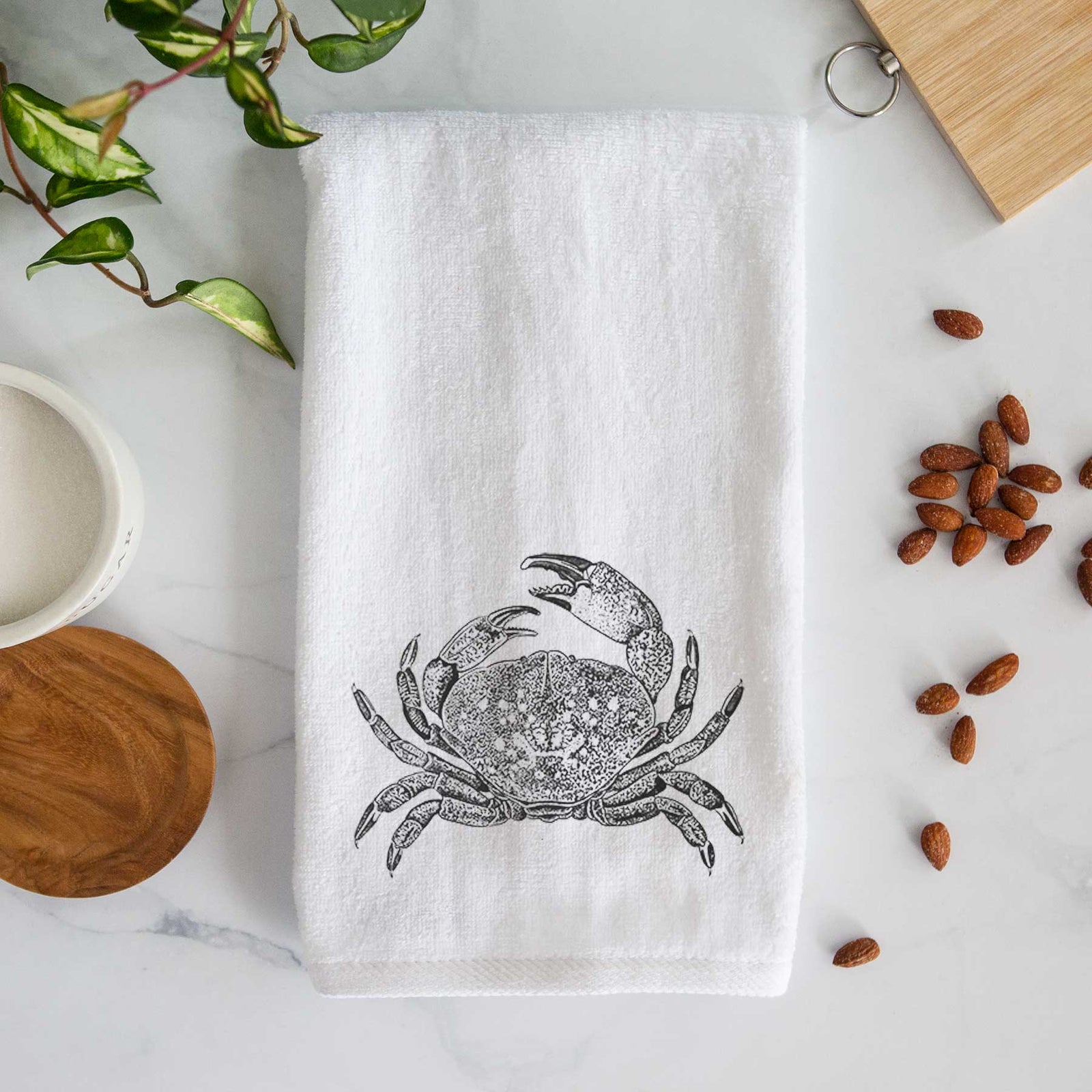 White hand towel printed with a detailed black ink illustration of a Dungeness crab with claws raised, seen from above.