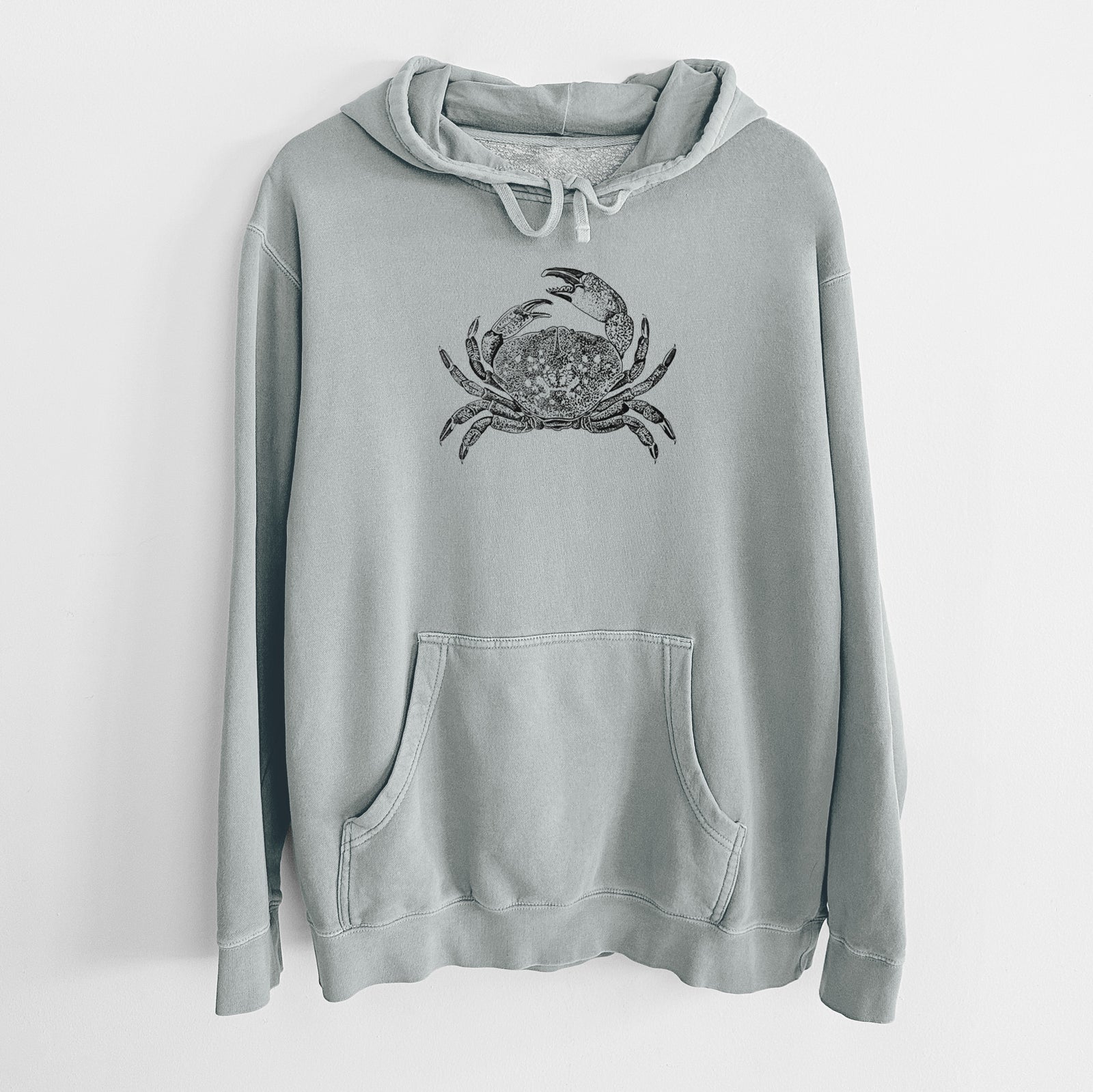 Sage green pigment dyed hoodie laid flat, printed with a detailed black ink illustration of a Dungeness crab with claws raised, seen from above.