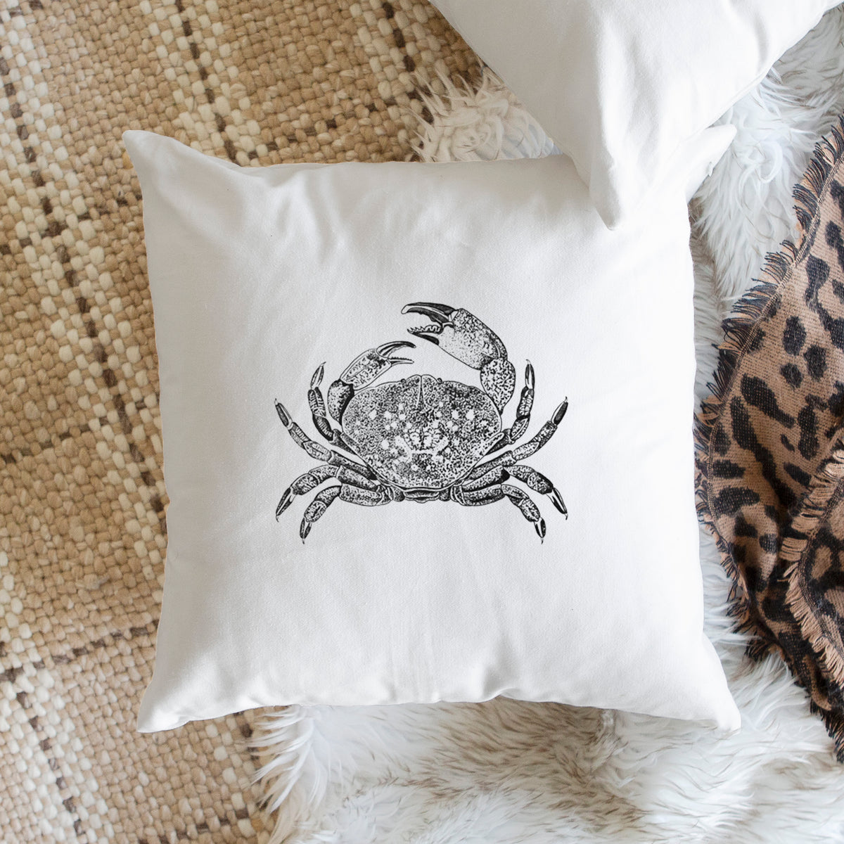 White pillow cover printed with a detailed black ink illustration of a Dungeness crab with claws raised, seen from above, on a woven chair.