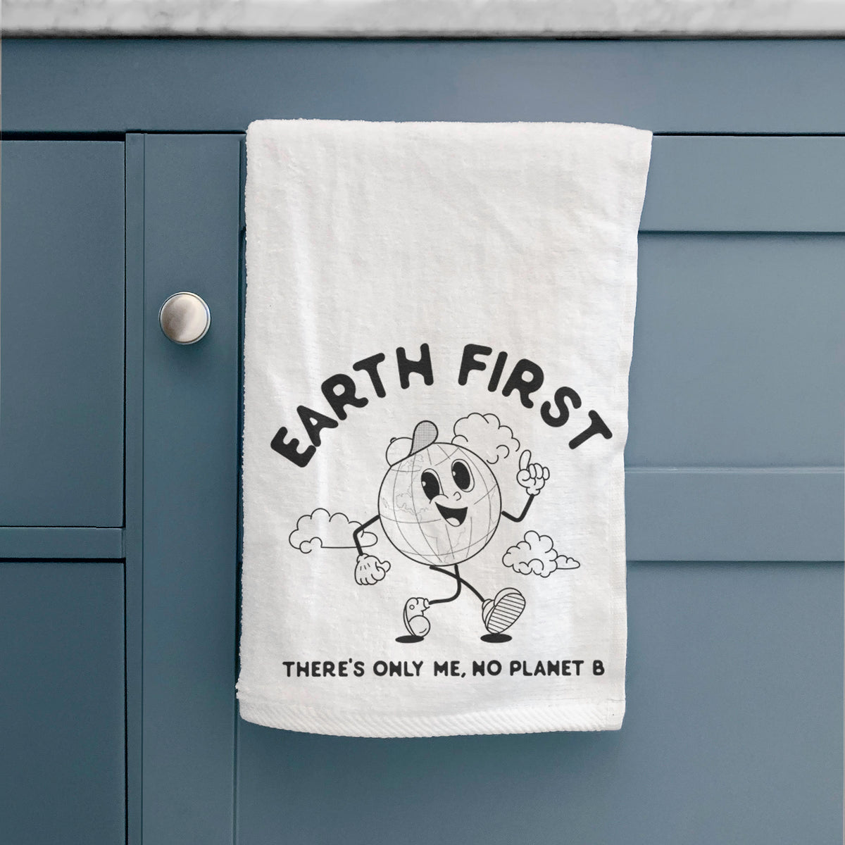 White hand towel printed with a cheerful cartoon Earth running, with the words Earth First and There's Only Me, No Planet B, hanging on a cabinet door.
