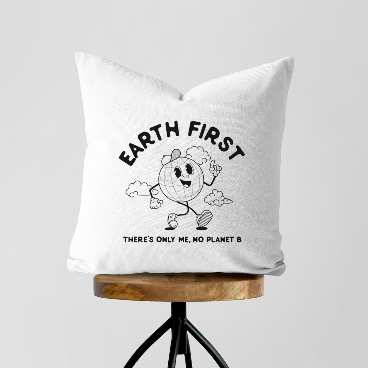 White pillow cover printed with a cheerful cartoon Earth running, with the words Earth First and There's Only Me, No Planet B, on a wooden stool.