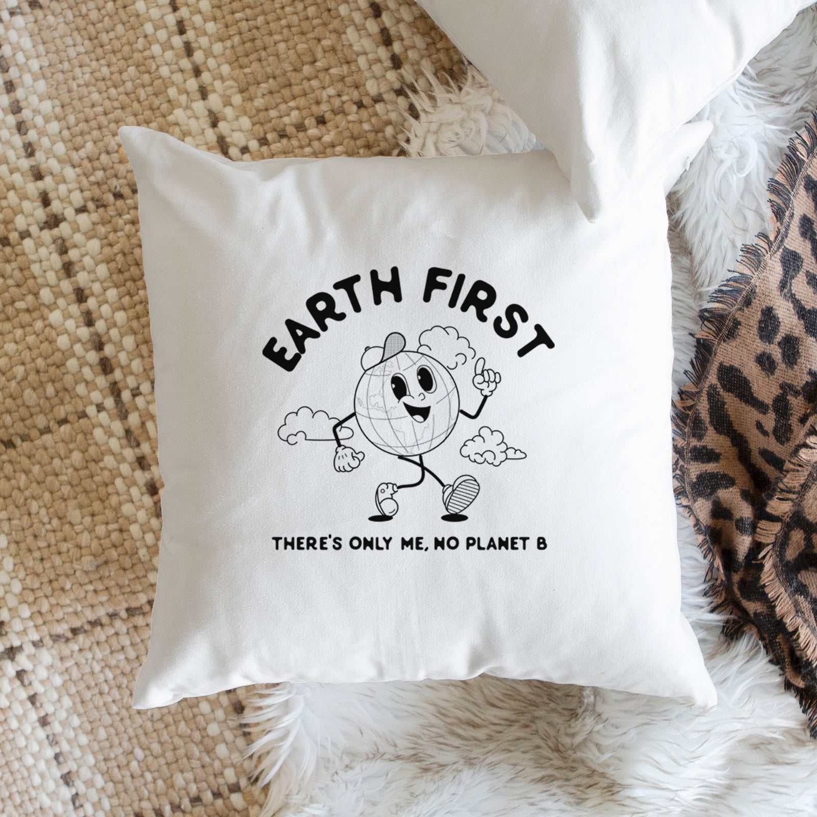 White pillow cover printed with a cheerful cartoon Earth running, with the words Earth First and There's Only Me, No Planet B, on a bench beside plants.