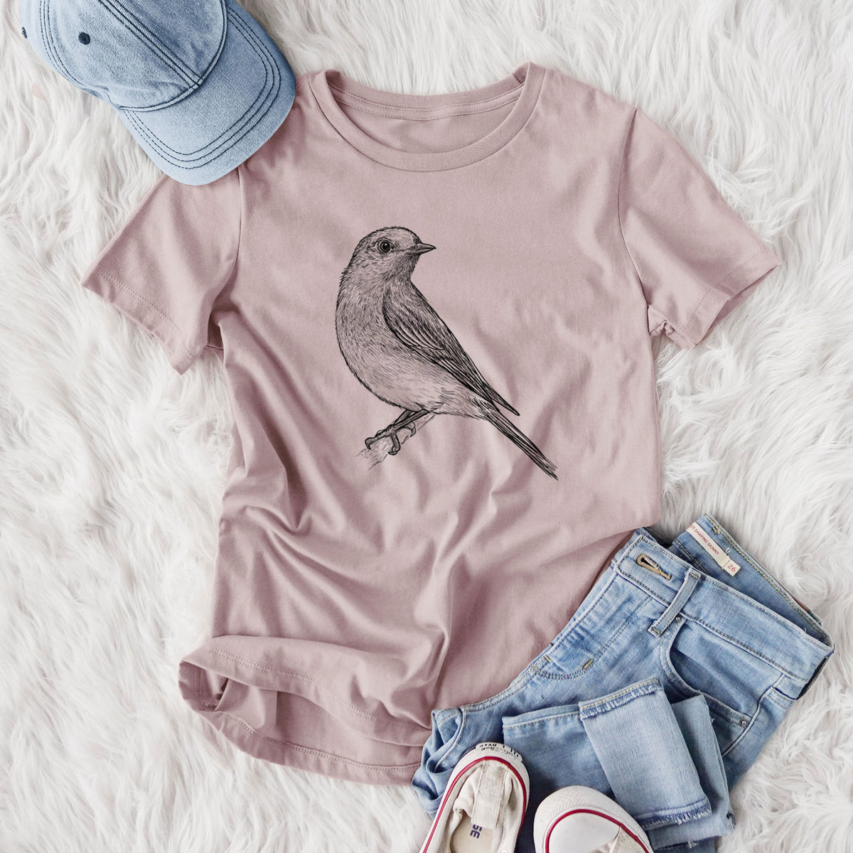 Women's relaxed fit cotton t-shirt printed with a detailed black ink sketch of an eastern bluebird perched on a branch, styled flat on a white faux fur rug with jeans.
