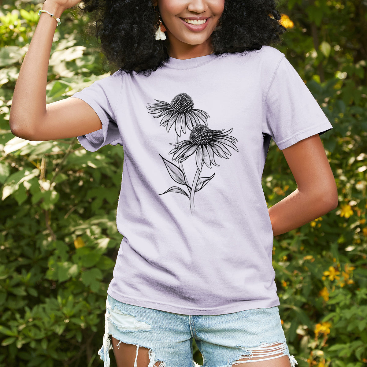 Woman wearing a Comfort Colors t-shirt printed with a black ink line drawing of two coneflowers on tall stems, outdoors.