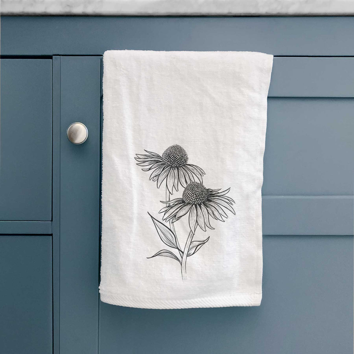White hand towel printed with a black ink line drawing of two coneflowers on tall stems, hanging on a cabinet door.