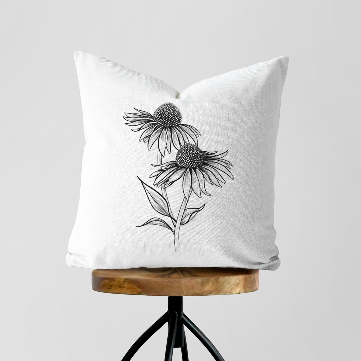 White pillow cover printed with a black ink line drawing of two coneflowers on tall stems, on a wooden stool.