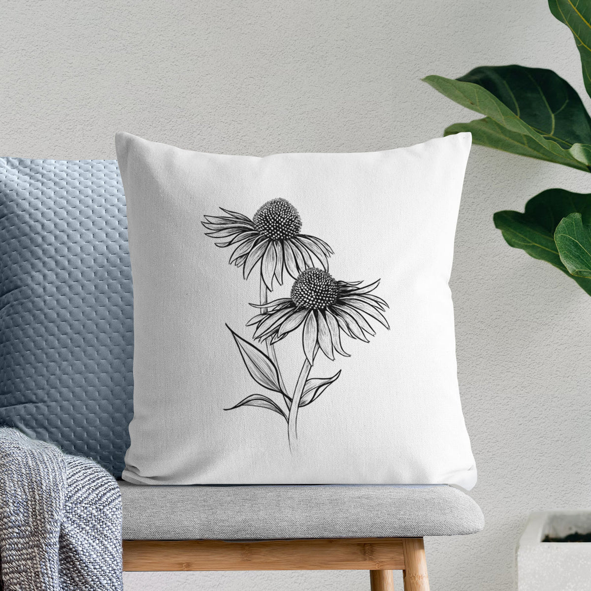 White pillow cover printed with a black ink line drawing of two coneflowers on tall stems, on a bench beside plants.