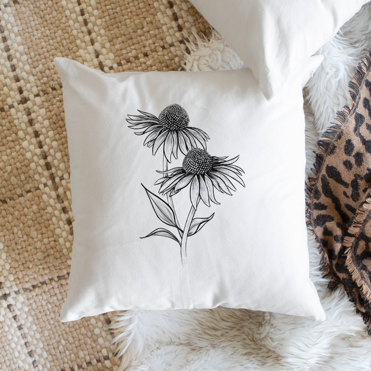 White pillow cover printed with a black ink line drawing of two coneflowers on tall stems, on a woven chair.