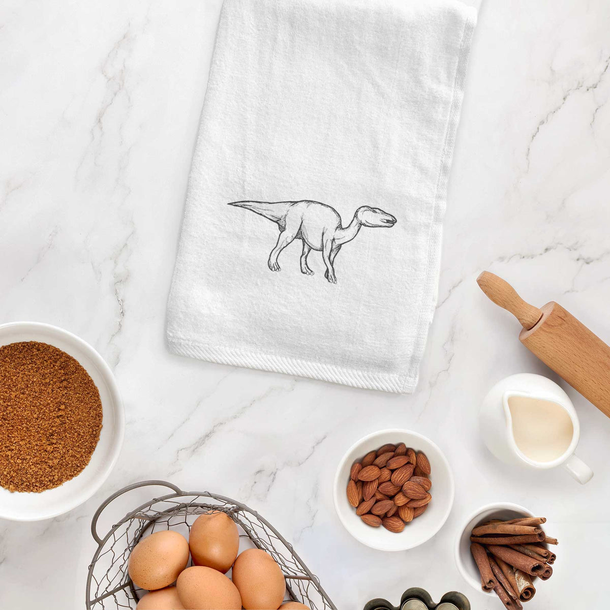 White hand towel printed with a black ink illustration of an Edmontosaurus walking, hanging on a cabinet door.