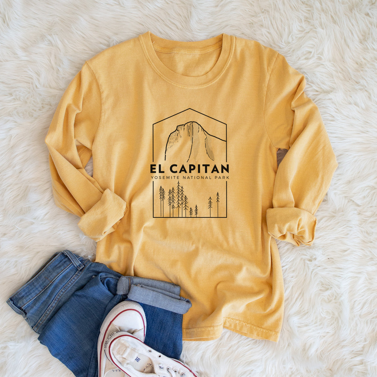 Golden wheat yellow Comfort Colors long sleeve shirt printed with a black line art badge of El Capitan rising above a pine forest, with the words El Capitan, Yosemite National Park, shown in a lifestyle photo.
